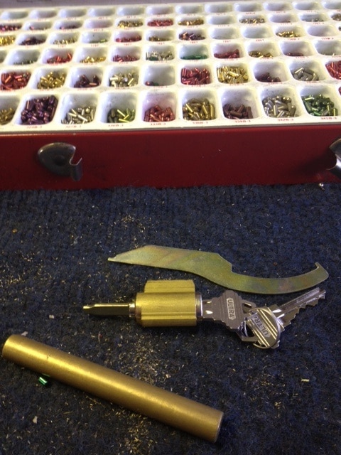 image of a lock cylinder with a key in it, rekeying tools, and case of lock cylinder pins.